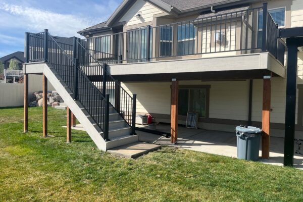 Two-story deck with upper balcony and staircase connecting levels in a backyard setting